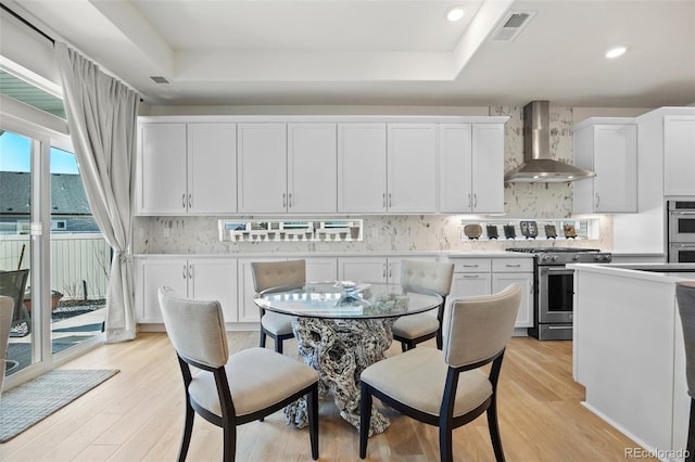 kitchen featuring tasteful backsplash, appliances with stainless steel finishes, light wood-style flooring, and wall chimney range hood