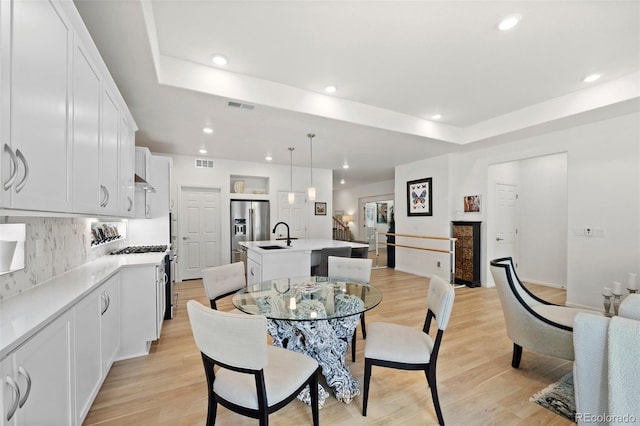 dining room with a tray ceiling, visible vents, and light wood-type flooring