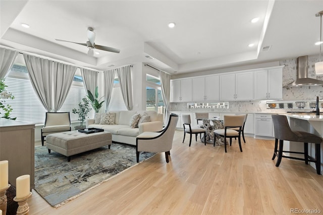 living area with visible vents, recessed lighting, ceiling fan, light wood-style floors, and a raised ceiling