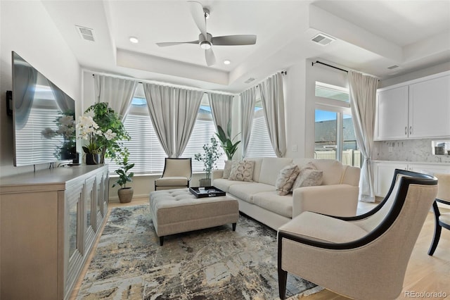 living area featuring visible vents, a raised ceiling, a healthy amount of sunlight, and a ceiling fan