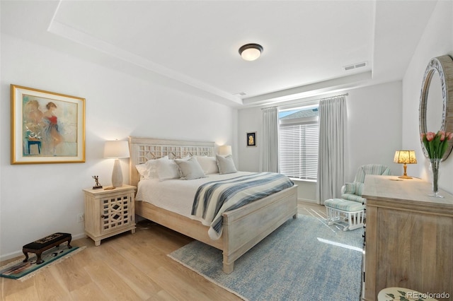 bedroom with a raised ceiling, light wood-style flooring, baseboards, and visible vents