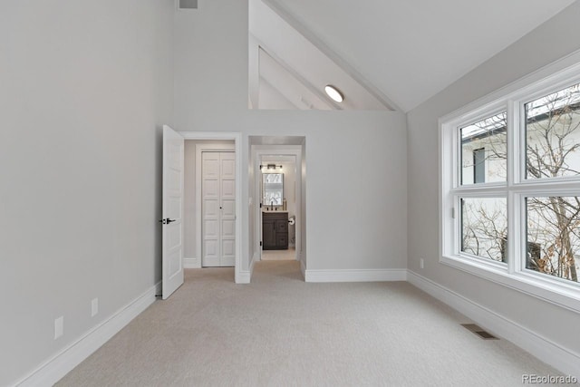 unfurnished bedroom featuring light carpet, high vaulted ceiling, and connected bathroom