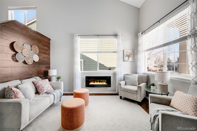 living room featuring a towering ceiling, baseboards, light colored carpet, and a glass covered fireplace