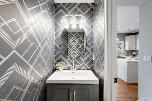 bathroom featuring recessed lighting, wood finished floors, vanity, backsplash, and crown molding