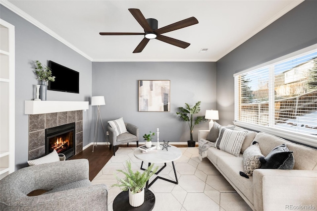 living area featuring a ceiling fan, a tile fireplace, crown molding, and baseboards