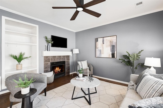 living area featuring built in shelves, visible vents, wood finished floors, a tile fireplace, and baseboards