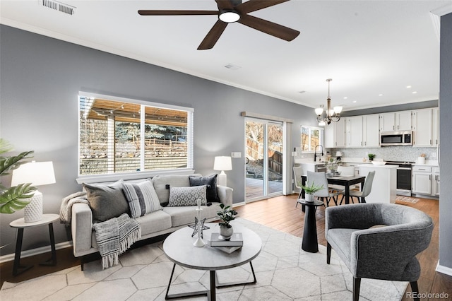 living area with light wood finished floors, baseboards, visible vents, and crown molding