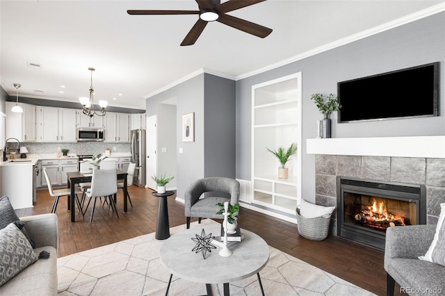 living room featuring built in shelves, a tile fireplace, crown molding, and wood finished floors