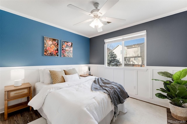 bedroom with ornamental molding, a ceiling fan, a wainscoted wall, and wood finished floors