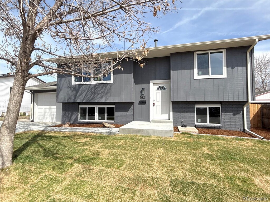 raised ranch with a front yard, an attached garage, and brick siding