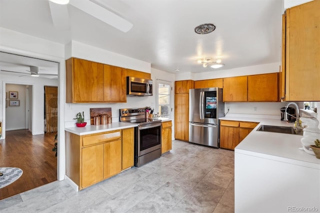 kitchen featuring a sink, a ceiling fan, light countertops, appliances with stainless steel finishes, and brown cabinets