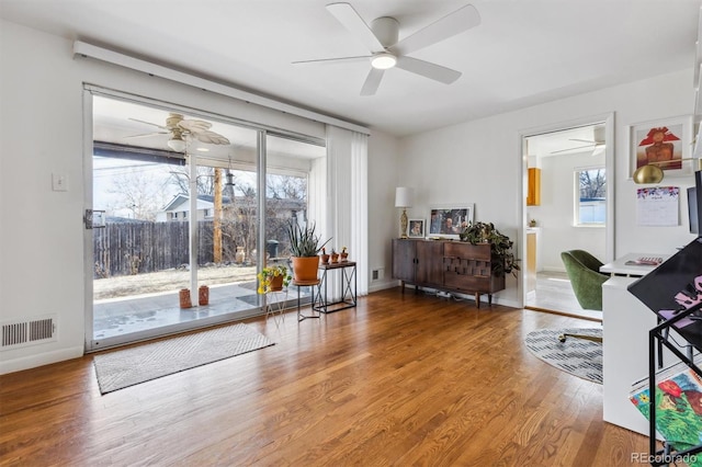 living area with baseboards, visible vents, ceiling fan, and wood finished floors