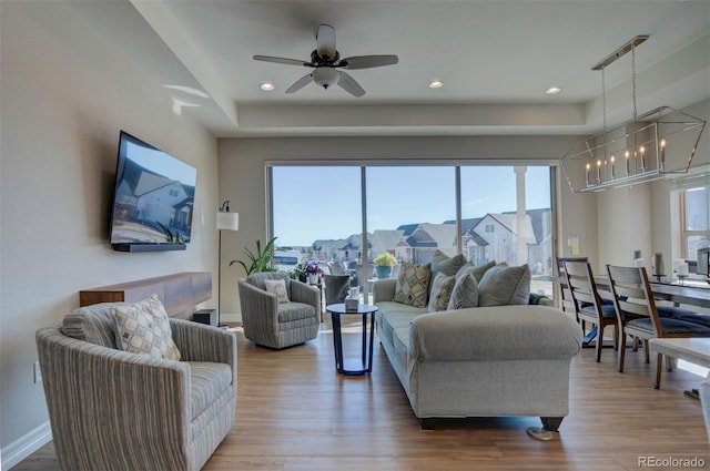 living room featuring a raised ceiling, ceiling fan with notable chandelier, wood finished floors, recessed lighting, and baseboards