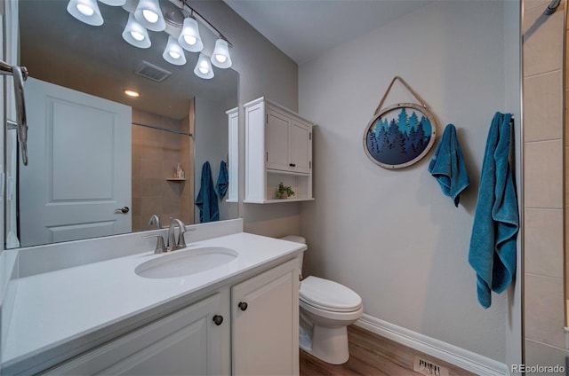 bathroom with visible vents, baseboards, toilet, a tile shower, and vanity