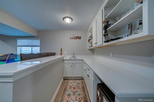 interior space featuring open shelves, a peninsula, a sink, light countertops, and white cabinetry