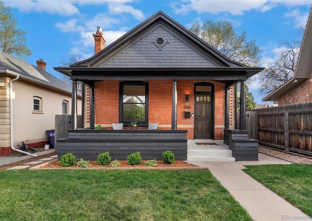 bungalow featuring brick siding, fence, covered porch, and a chimney