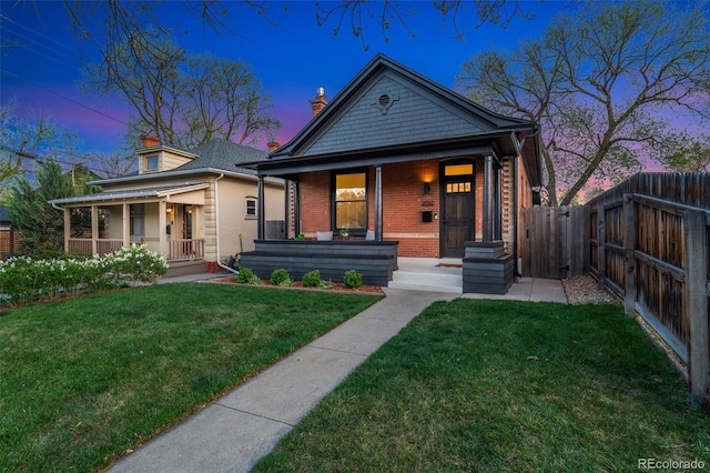 view of front of property featuring covered porch, a chimney, a front yard, brick siding, and fence