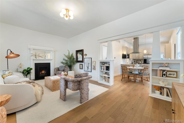 living area featuring a fireplace with flush hearth, baseboards, and light wood-style flooring
