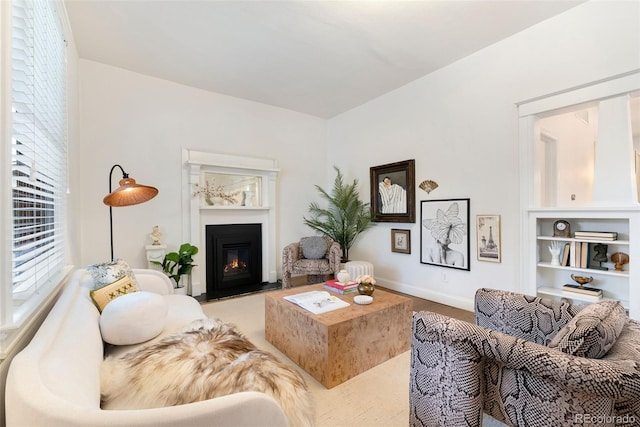 living area featuring a glass covered fireplace, baseboards, built in shelves, and wood finished floors