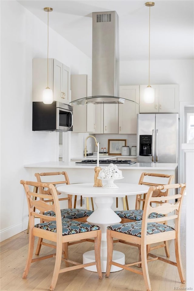 kitchen with light wood-style floors, light countertops, island exhaust hood, appliances with stainless steel finishes, and decorative light fixtures
