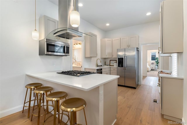 kitchen with a peninsula, a breakfast bar area, island exhaust hood, a sink, and appliances with stainless steel finishes