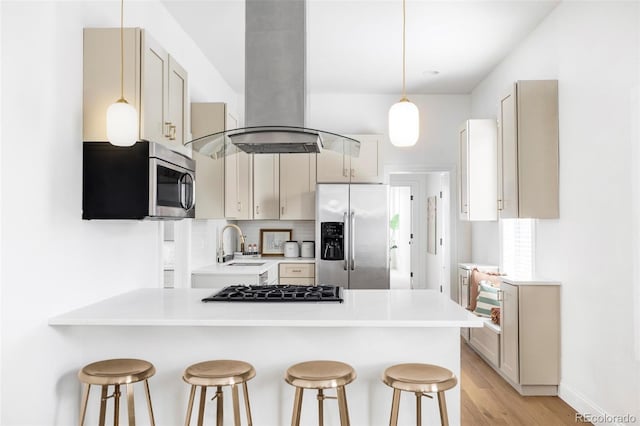 kitchen with a peninsula, a kitchen bar, light countertops, island exhaust hood, and stainless steel appliances
