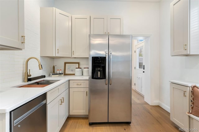 kitchen featuring decorative backsplash, appliances with stainless steel finishes, a sink, light countertops, and light wood-style flooring
