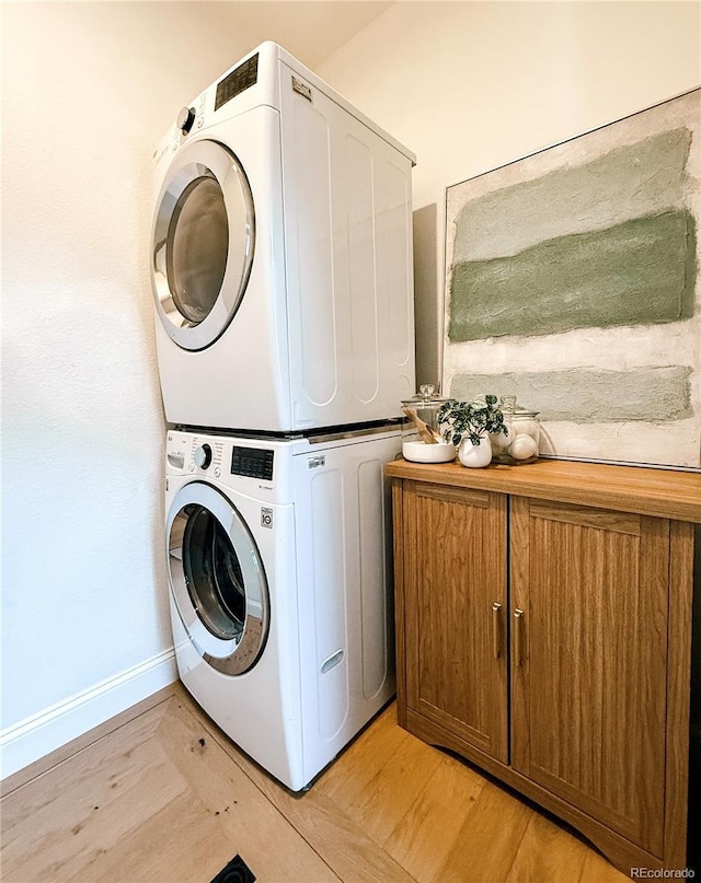 laundry room featuring baseboards, stacked washer and clothes dryer, light wood-style flooring, and cabinet space