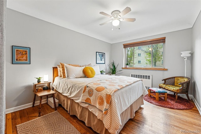 bedroom featuring a ceiling fan, baseboards, wood finished floors, and radiator