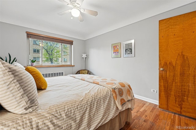 bedroom featuring baseboards, a ceiling fan, radiator heating unit, and wood finished floors