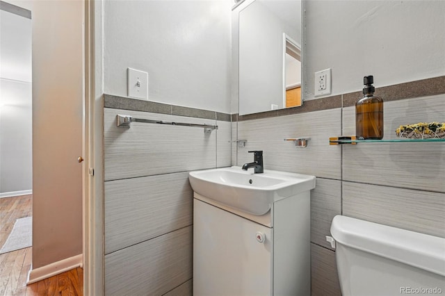 half bathroom with vanity, wood finished floors, toilet, and tile walls