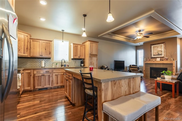 kitchen with stainless steel fridge, hanging light fixtures, a kitchen island, dark hardwood / wood-style floors, and a tray ceiling