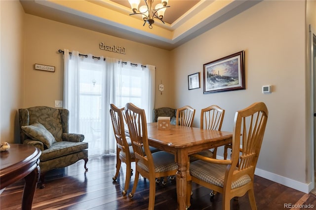 dining space with dark wood-type flooring, a tray ceiling, and an inviting chandelier