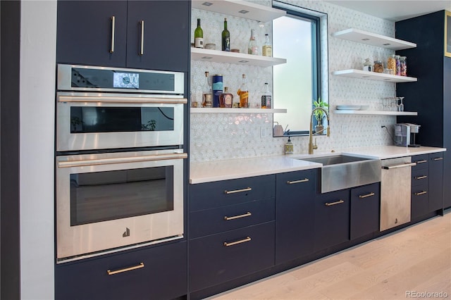 kitchen featuring blue cabinetry, sink, stainless steel double oven, tasteful backsplash, and light hardwood / wood-style flooring