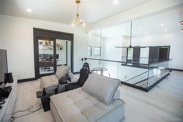 living room featuring ceiling fan with notable chandelier, light hardwood / wood-style floors, and a wealth of natural light