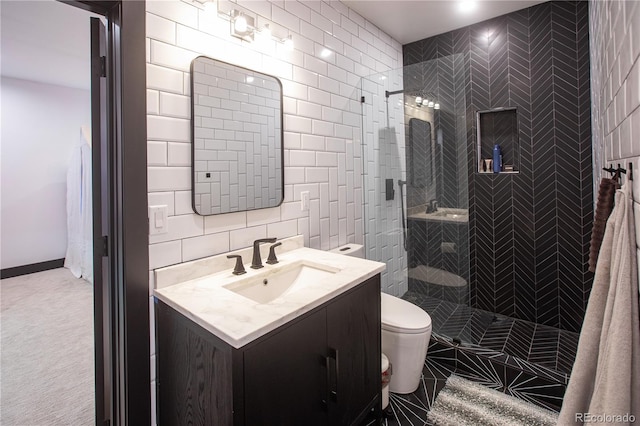 bathroom with a tile shower, vanity, toilet, and tile walls