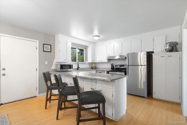 2502 S Lima St, Aurora, CO 80014 - kitchen with appliances with stainless steel finishes, under cabinet range hood, light wood-style flooring, white cabinets, and a breakfast bar area