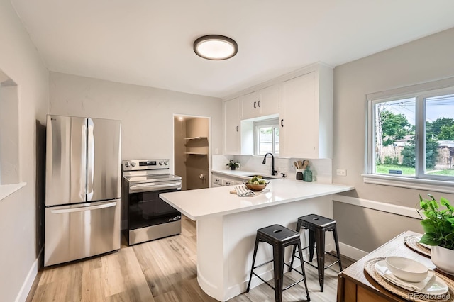 1237 Tamarac St, Denver, CO 80220 - kitchen with appliances with stainless steel finishes, light countertops, a peninsula, white cabinetry, and light wood-style flooring