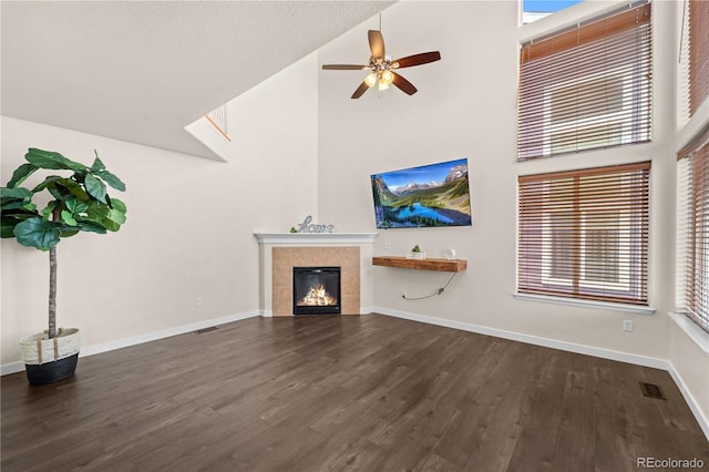 unfurnished living room featuring dark wood-type flooring, a fireplace, ceiling fan, and a towering ceiling