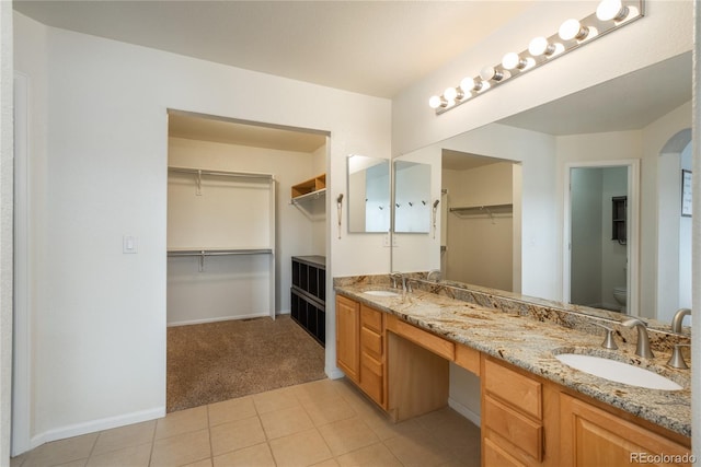 bathroom featuring toilet, baseboards, double vanity, and a sink