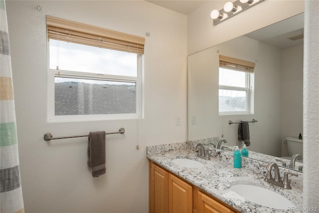bathroom featuring toilet, double vanity, and a sink