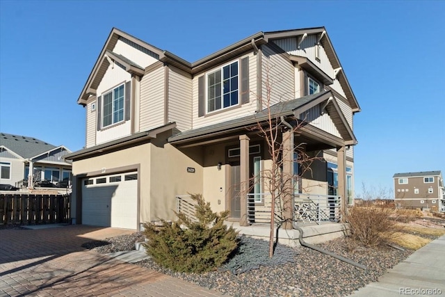 craftsman-style home with decorative driveway, an attached garage, fence, and stucco siding