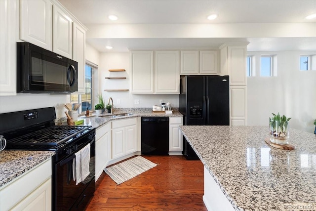 kitchen featuring dark wood-style floors, light stone counters, white cabinets, a sink, and black appliances