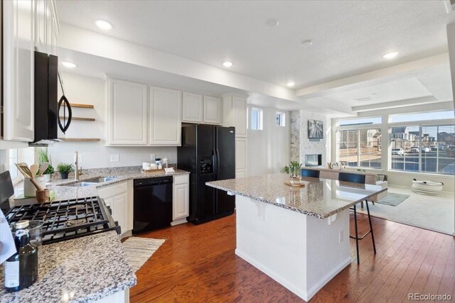 kitchen featuring dark wood finished floors, a raised ceiling, black appliances, open shelves, and a sink