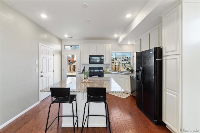 kitchen featuring black appliances, dark wood finished floors, light stone countertops, and white cabinets