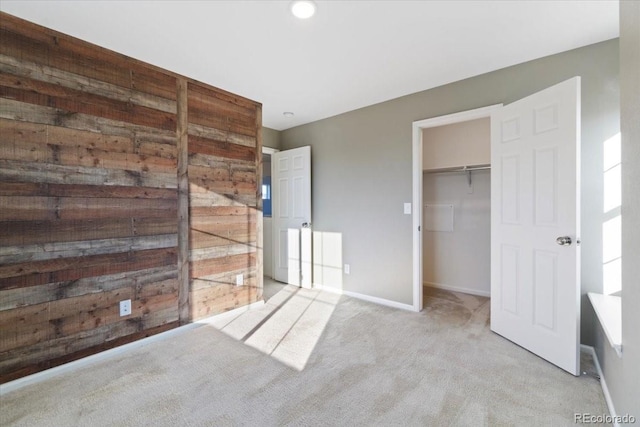 unfurnished bedroom featuring wood walls, baseboards, a spacious closet, a closet, and carpet