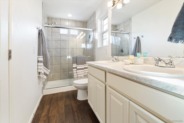 bathroom featuring double vanity, wood finished floors, a sink, and a shower stall