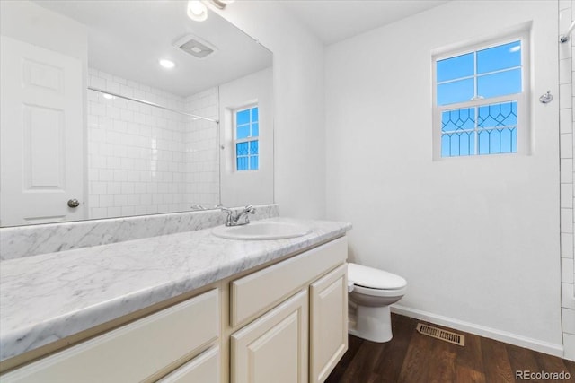 bathroom with baseboards, toilet, wood finished floors, a tile shower, and vanity