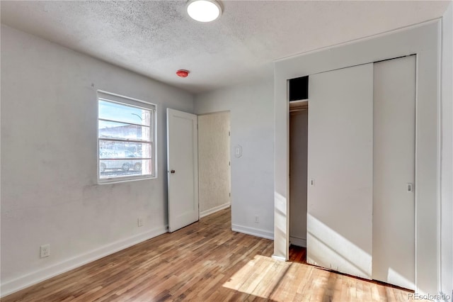 unfurnished bedroom with light hardwood / wood-style floors, a textured ceiling, and a closet