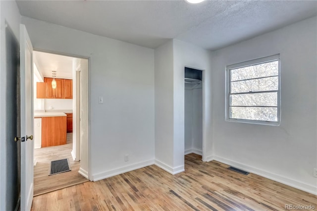 unfurnished bedroom featuring a textured ceiling, a closet, and light hardwood / wood-style flooring